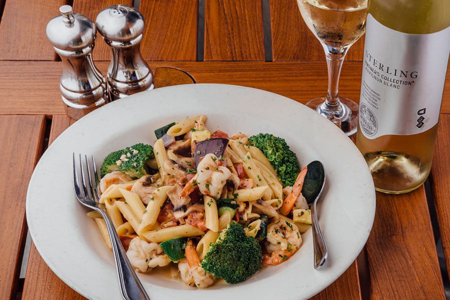 A bowl of pasta, shrimp, and vegetables and a bottle of white wine