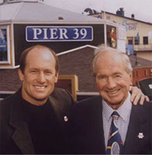 Scooter Simmons (left) and his father and patriarch Warren Simmons (right) in front of the PIER 39 sign