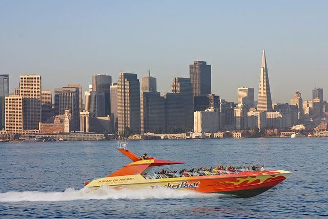 A boat speeds through the water with San Francisco in the background